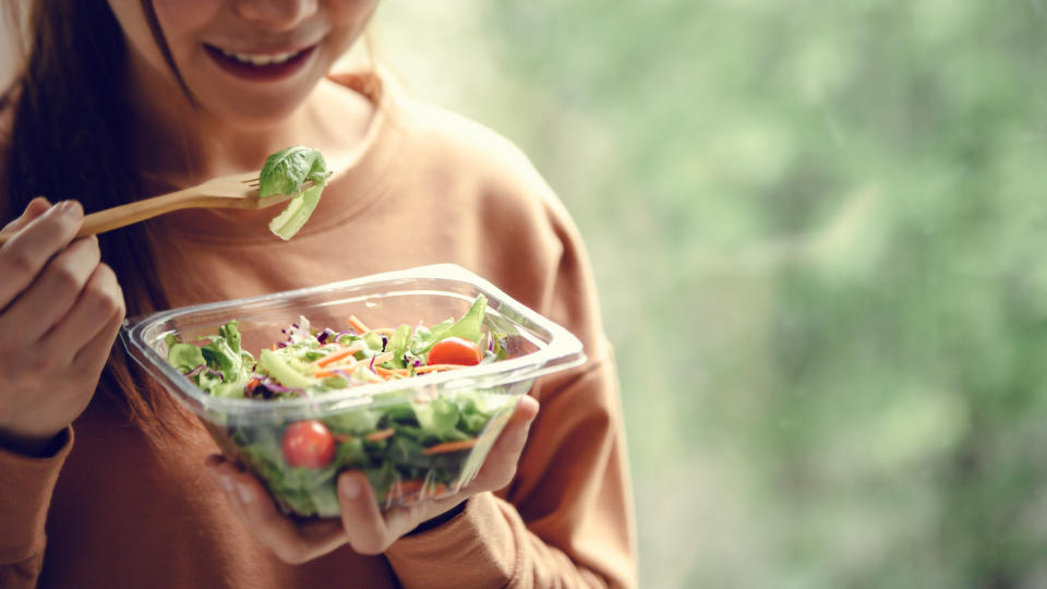 closeup woman eating healthy food salad, focus on salad and fork