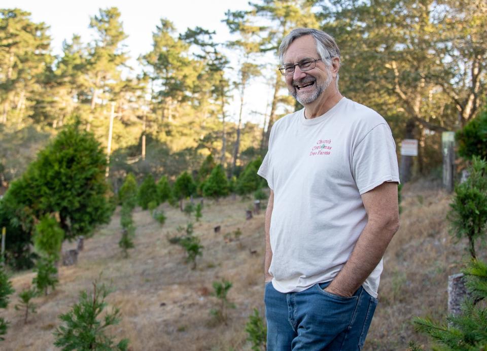 Glenn Church smiles as he stands on a hill surrounded by his Christmas trees on Nov. 22, 2019.