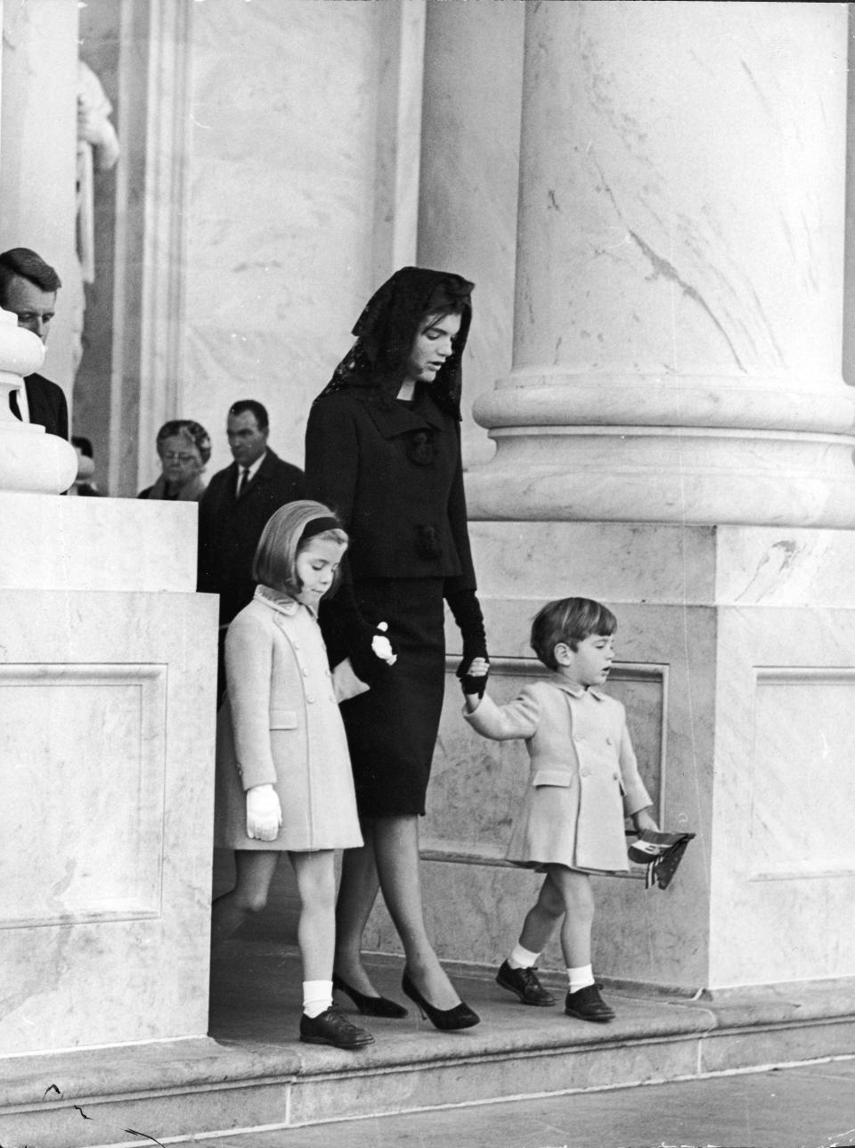 26th November 1963, First Lady Jacqueline Kennedy (1929 - 1994) holds the hands of her two children, John Jr (1960 - 1999) and Caroline, as they leave the White House to attend the Lying-in-State of assassinated President John F Kennedy at the Capitol, Washington, D C. Rober (Photo by Express/Getty Images)