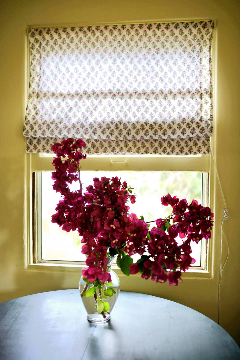 dining room with round table, window with patterned shade, and bougainvillea in vase