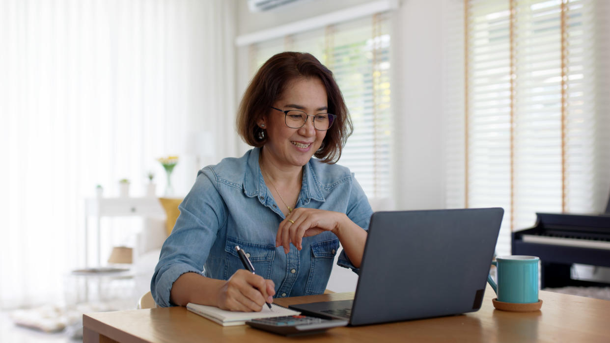 Woman smiling while writing notes and looking at laptop