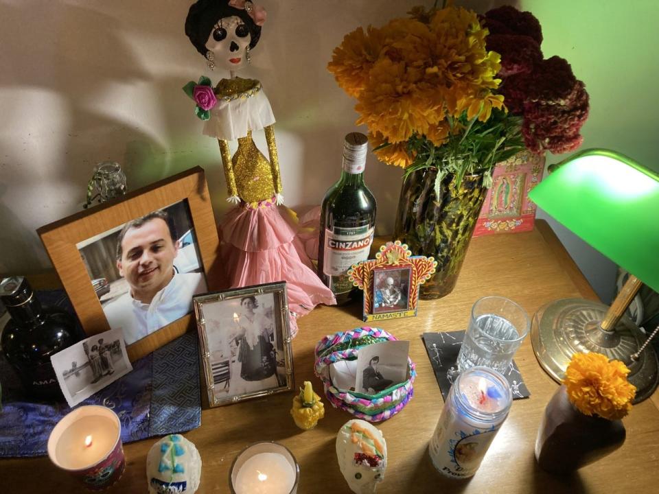 Carli Pierson's 2022 Day of the Dead altar: pictures of her grandparents, mother-in-law and  brother-in-law; fresh marigolds; skulls made out of sugar; a candle; a paper and cardboard Catrina (skeleton doll); a glass of water; a bottle of Cinzano that her late mother-in-law, Juana, liked to drink.