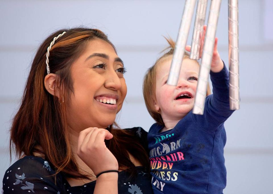 Roxanna Campos-Sosa, a teacher at the Little School of Hillsborough, watches as Mackenzie, 1, plays with wind chimes on Thursday, April 18, 2024, in Hillsborough, N.C.