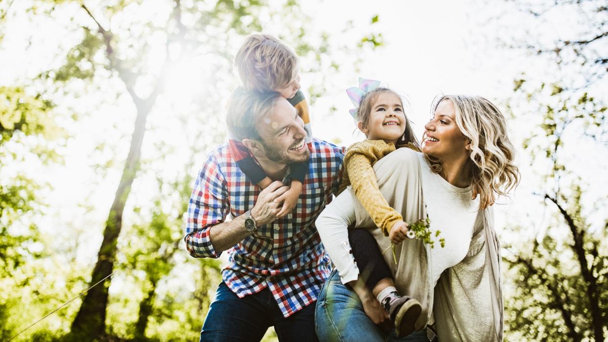 Low angle view of happy parents having fun while piggybacking their small kids in nature.