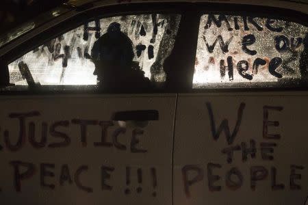 A protester takes refuge from snowfall while sitting outside the Ferguson Police Station in Missouri November 26, 2014. REUTERS/Adrees Latif