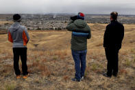 David Marks, center, uses a borrowed pair of binoculars to see how his home in Superior, Colo., fared as smoke rises in the distance on Friday, Dec. 31, 2021. A wind-whipped wildfire tore through the area Thursday, and authorities fear more than 500 homes were destroyed. (AP Photo/Thomas Peipert)
