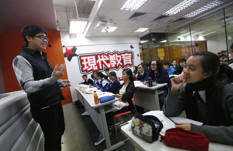 In this Dec. 9, 2013 photo, English grammar tutor Tony Chow, left, gives a lesson to his students in a classroom of Modern Education in Hong Kong. The 30-year-old teaches English grammar to thousands of secondary school pupils, who attend his after-school lessons or watch video replays of them at Modern Education’s 14 branches. Chow is a celebrity tutor in Hong Kong, where there’s big money to be made offering extracurricular lessons to parents desperately seeking an edge for their children preparing for the city’s intense public entrance exam for university. (AP Photo/Kin Cheung)