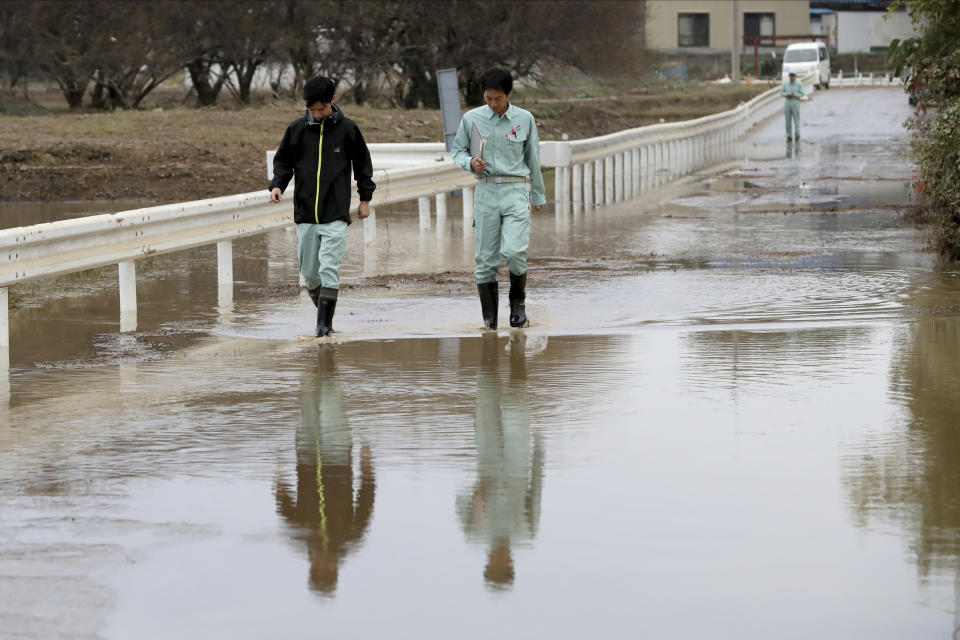 Workers survey a flooded street Monday, Oct. 14, 2019, in Kawagoe City, Japan. Rescue crews are digging through mudslides and searching near swollen rivers for missing people after Typhoon Hagibis caused serious damage in central and northern Japan. Dozens of people are dead or missing. (AP Photo/Eugene Hoshiko)