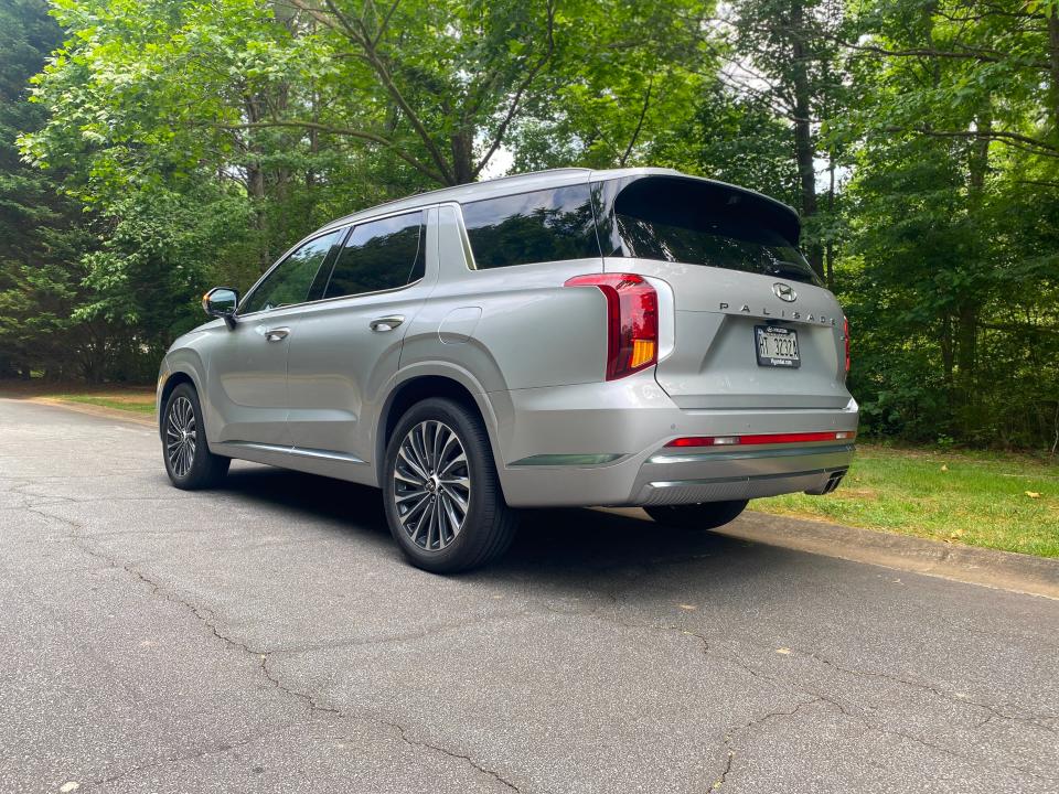 The rear three-quarters view of a silver Hyundai Palisade SUV parked in front of a wooded area.