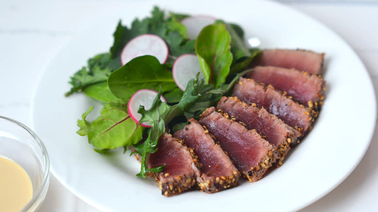 Tuna steak on a plate with greens and dipping sauce on the side