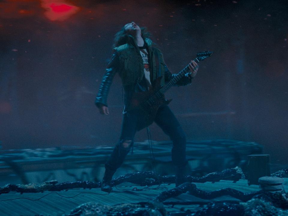 eddie munson playing guitar in stranger things, standing on top of a roof in the upside down and throwing his head back