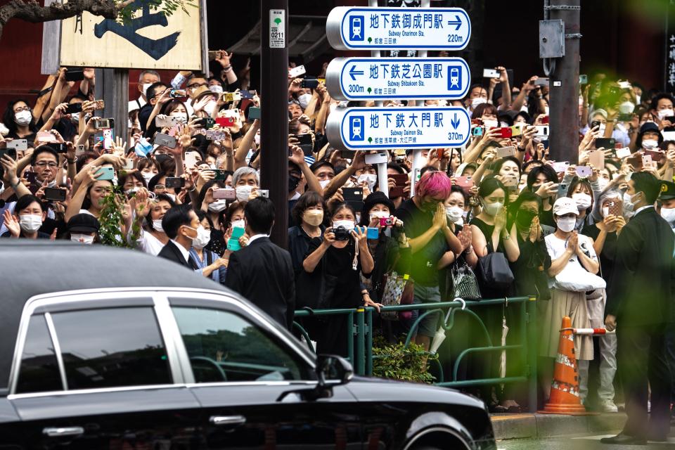 TOPSHOT - People watch the hearse transporting the body of late former Japanese prime minister Shinzo Abe as it leaves Zojoji Temple in Tokyo on July 12, 2022. (Photo by Philip FONG / AFP) (Photo by PHILIP FONG/AFP via Getty Images)