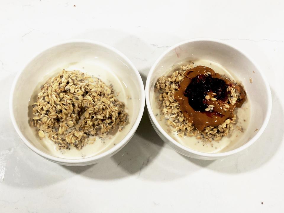 Two white bowls of overnight oats on a white countertop. The bowl on the right has peanut butter and raspberry preserves on top.