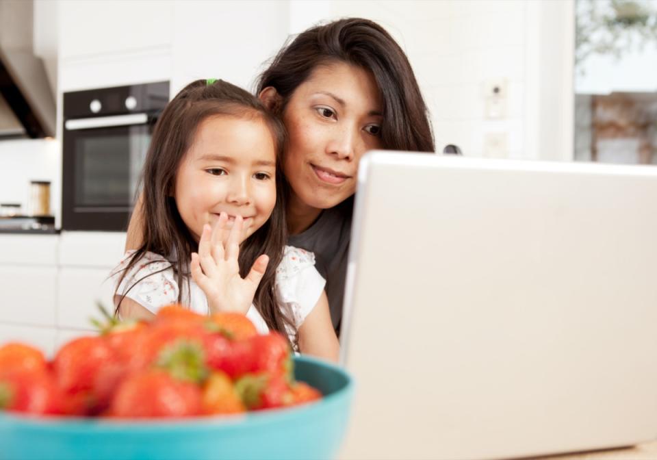 Mother and daughter using computer, waving while in a live video chat