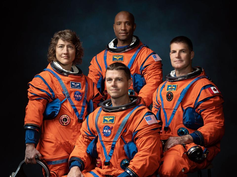 four astronauts in orange spacesuits pose for portrait