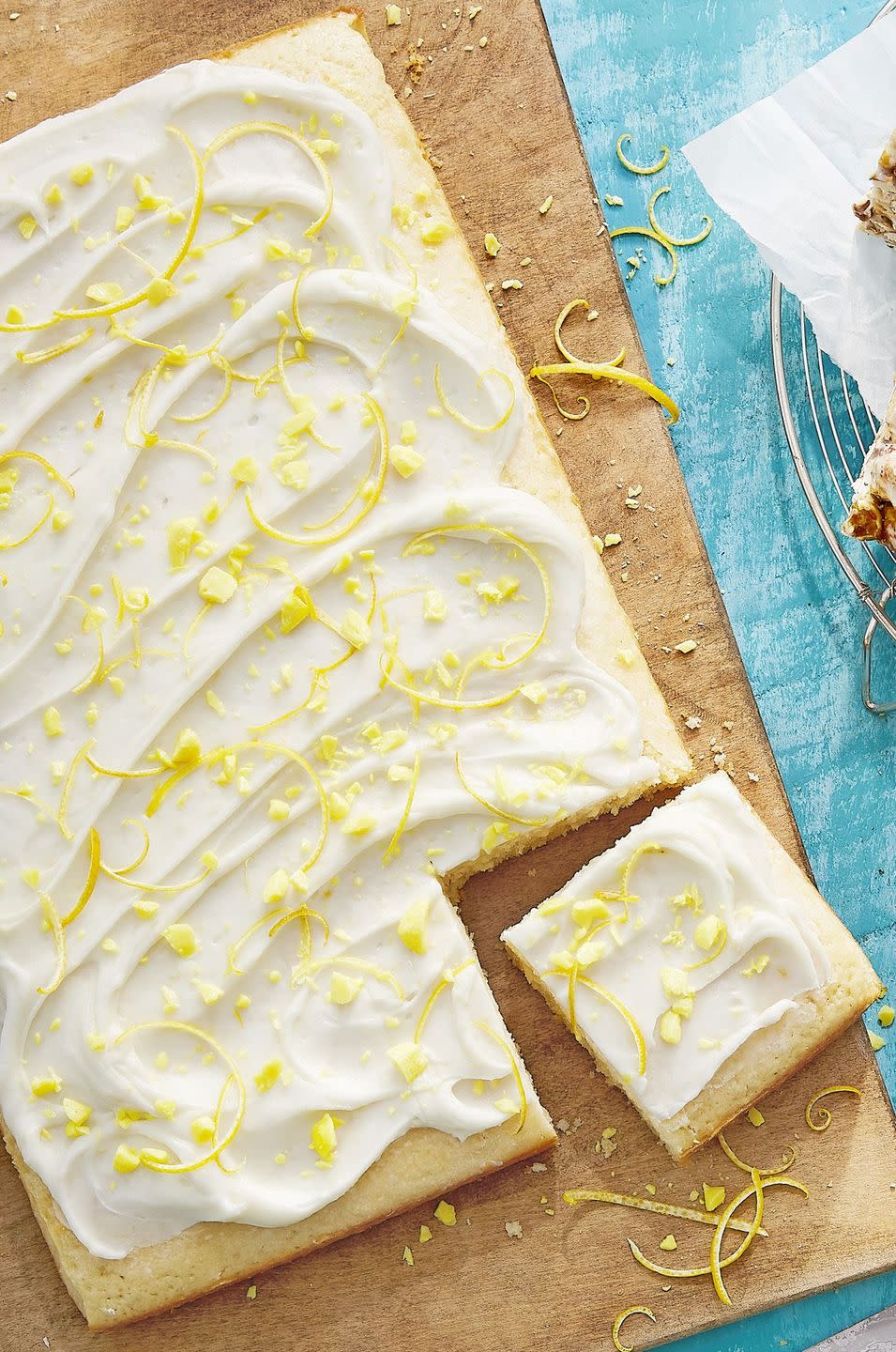 dukes lemon drop sheet cake with crushed lemon drops and lemon zest on top and arranged on a wooden serving board with one square piece cut out