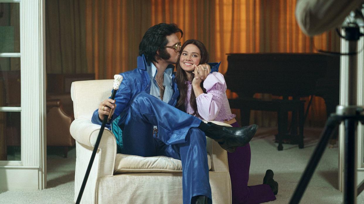 elvis presley sitting in a chair and kissing a smiling priscilla presley in a scene from the film priscilla