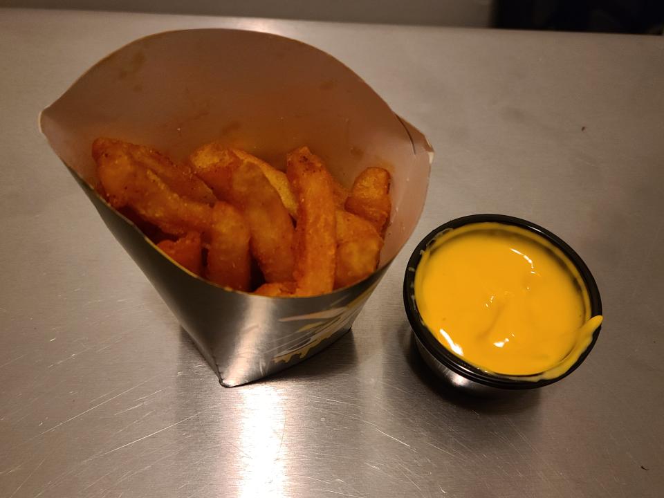 container of nacho fries next to a small container of nacho cheese sauce from taco bell