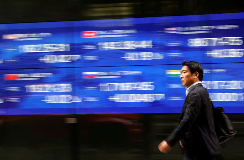 FILE PHOTO: A passerby walks past an electric monitor displaying various countries' stock price index outside a bank in Tokyo