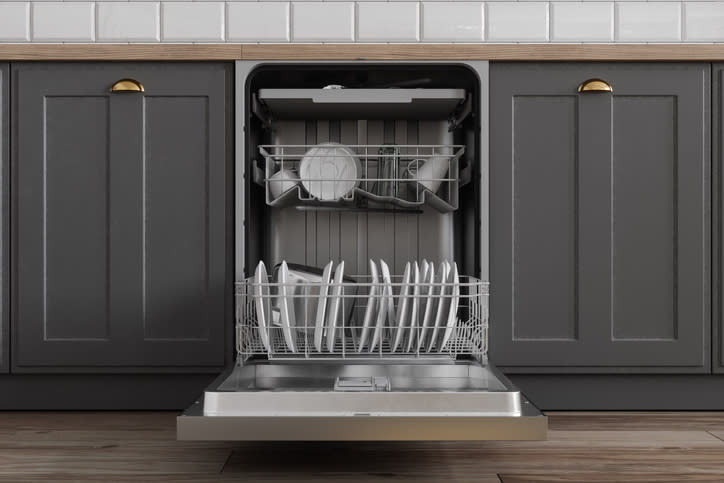 Open dishwasher with plates and cutlery, installed under a kitchen counter