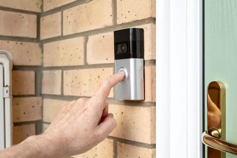 Visitor seen pressing the door bell button of a wireless smart home door bell which has an integrated camera and two-way audio. The door is a new, high security uPVC door.