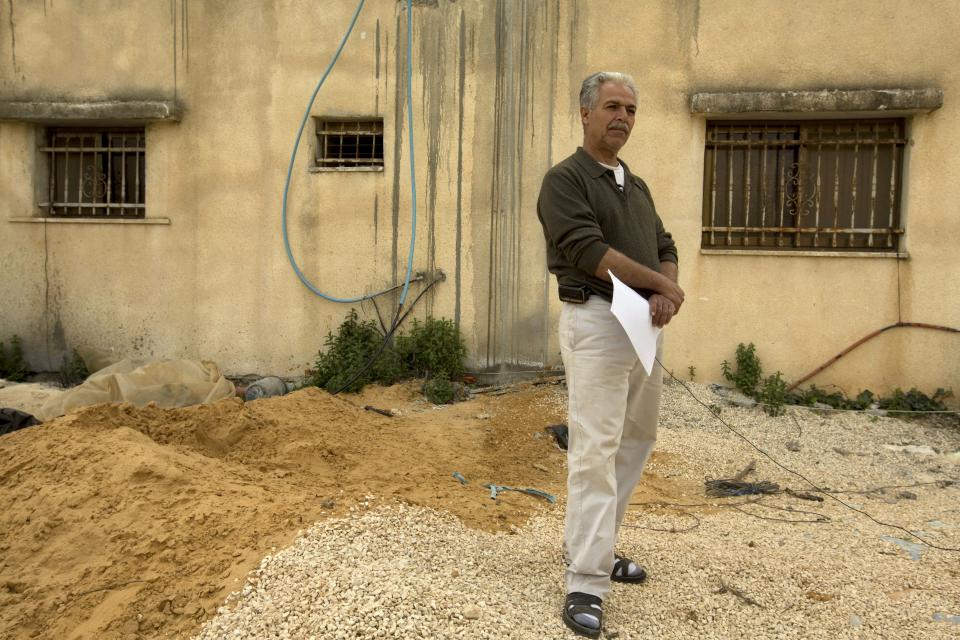 In this photo taken Monday, March 3, 2014, Palestinian Mohammed Awais, 53, stands in front of his house in the West Bank village of Lubban al-Sharkiyeh. Ahmed Awais has been desperate to get out of his parents' cramped home where he, his wife and three pre-school children share one room, sleeping on mattresses on the floor at night. (AP Photo/Sebastian Scheiner)