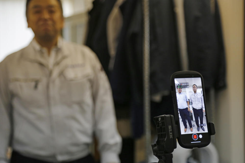 General Manager Tomohiko Kojima takes a TikTok video with CEO Daisuke Sakurai, as seen in the screen of the cell phone, at the Tokyo headquarters office of Daikyo Security Co. in Tokyo Monday, Aug. 22, 2022. They’re your run-of-the-mill Japanese “salarymen,” but the chief executive and general manager at a tiny Japanese security company are among the nation’s biggest TikTok stars, drawing 2.7 million followers and 54 million likes, and honored with awards as a trend-setter on the video-sharing app. (AP Photo/Yuri Kageyama)