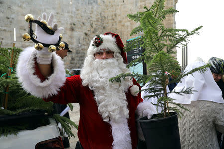 Israeli-Arab Issa Kassissieh, wearing a Santa Claus costume, holds a small tree and a bell during the annual Christmas tree distribution by the Jerusalem municipality in Jerusalem's Old City December 21, 2017. REUTERS/Ammar Awad