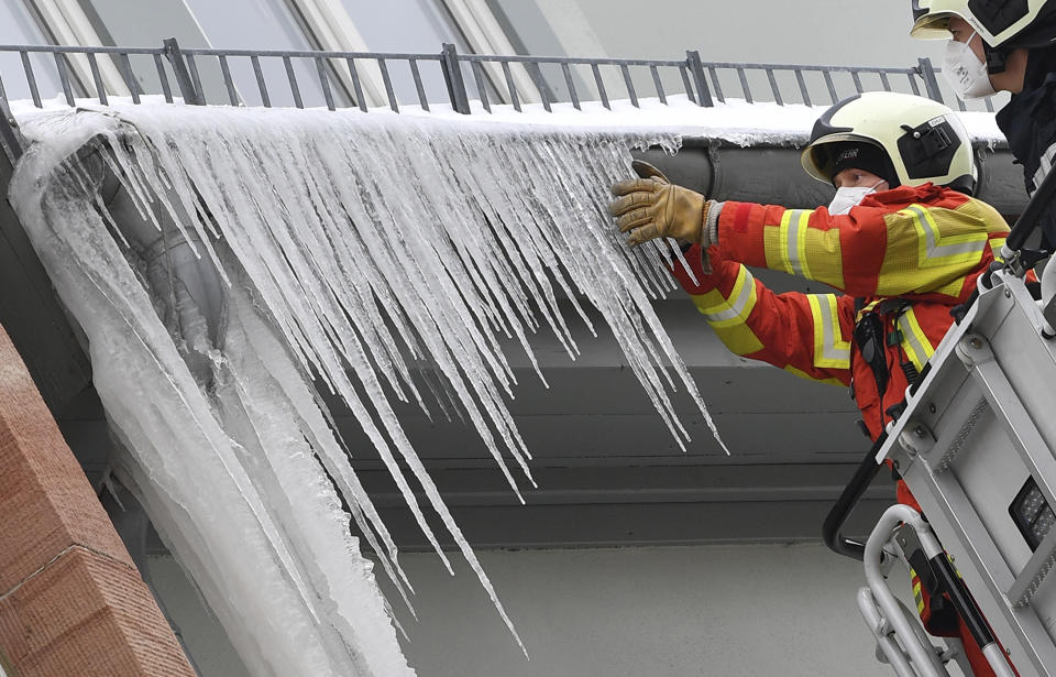 Firefighters break large icicles from the gutter of a house in the city centre of Erfurt, Germany, Thursday, Feb.11, 2021. Arctic polar air continues to cause severe frost in Germany. (Martin Schutt/dpa via AP)