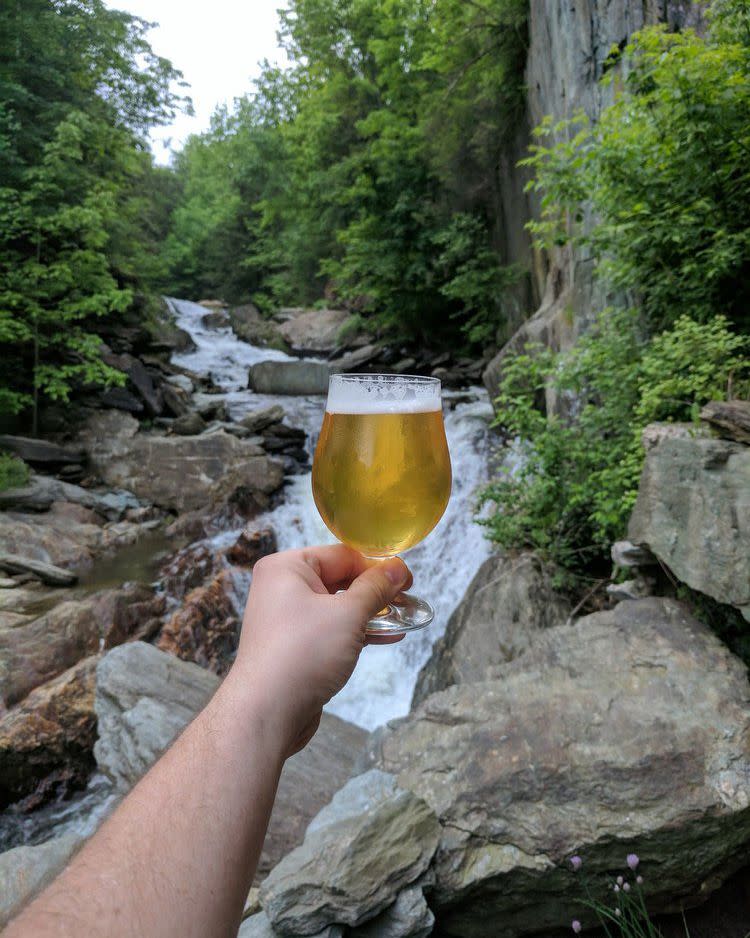 hand holding beer from hen of the wood in front of waterfall
