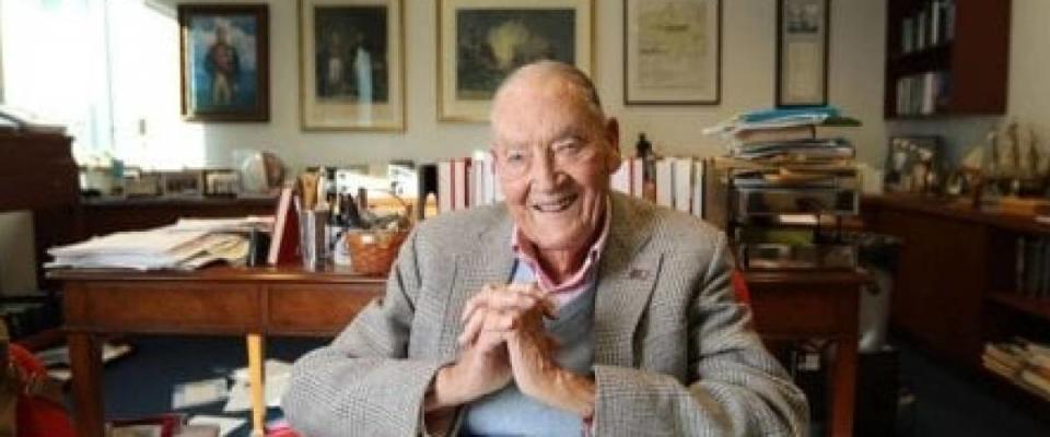 John Bogle poses for the camera, with a smile on his face and hands clasped.