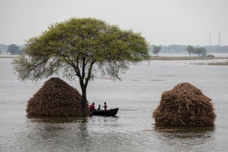 A woman with two children rows small boat in a flooded field in Bhagalpur district