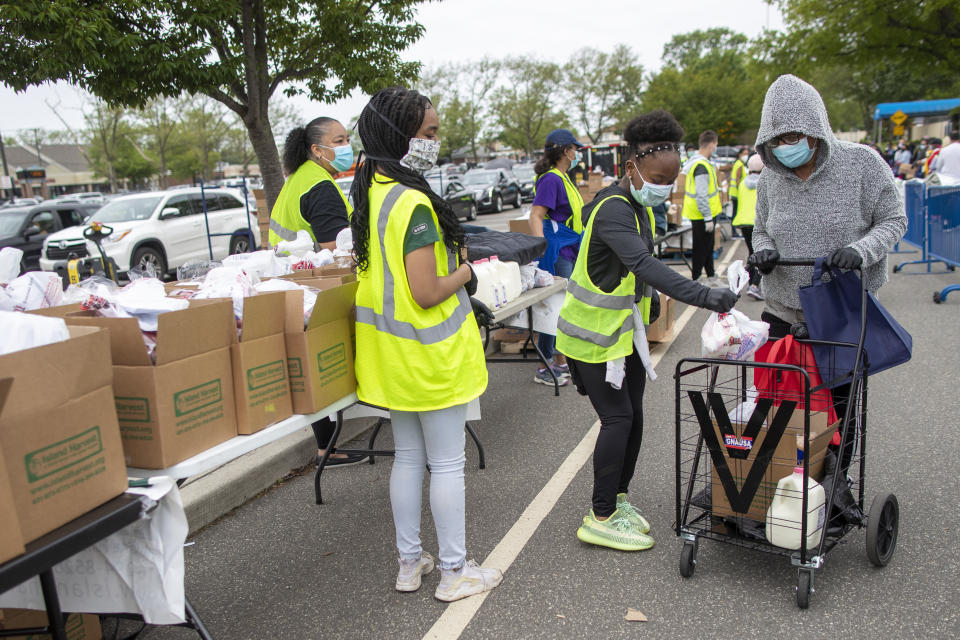 In this Thursday, May 28, 2020, photo, volunteers place groceries in Maria G.'s cart during a food distribution drive sponsored by Island Harvest Food Bank in Valley Stream, N.Y. The Valley Stream stream donations were just one of many events Island Harvest has conducted throughout the area recently. (AP Photo/Mary Altaffer)