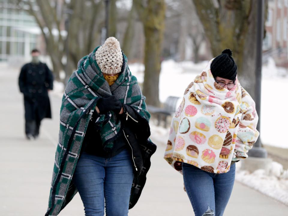 Two people wear blankets to keep warm while walking around in winter.