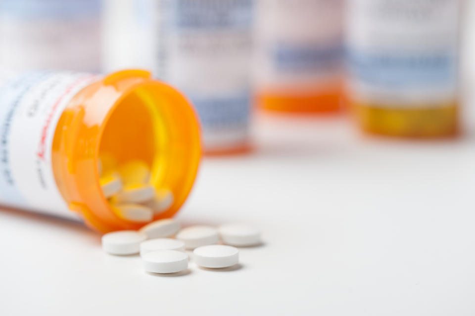 Prescription bottle with pills spilled out, in focus in the foreground, more bottles in the blurred background