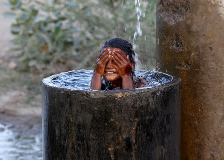FILE PHOTO: A girl bathes to cool off herself with water that is leaking from a broken pipe valve on a hot summer day on the outskirts of Ahmedabad, India, May 18, 2015. REUTERS/Amit Dave/File Photo