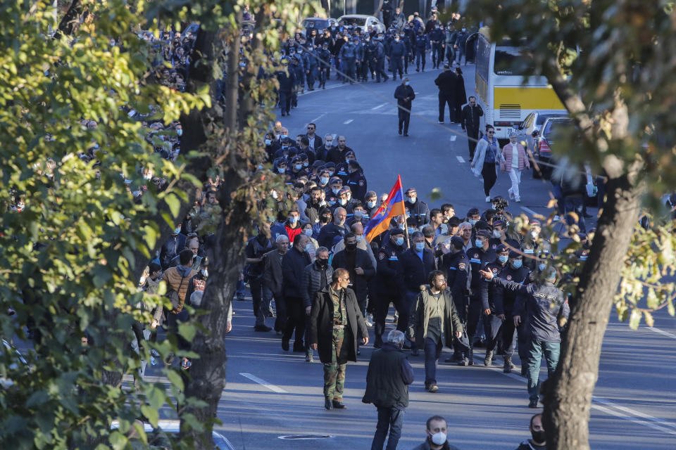 Protesters with an Armenian national flag followed by police, in the background, walk down a street during a protest against an agreement to halt fighting over the Nagorno-Karabakh region, in Yerevan, Armenia, Wednesday, Nov. 11, 2020. Thousands of people flooded the streets of Yerevan once again on Wednesday, protesting an agreement between Armenia and Azerbaijan to halt the fighting over Nagorno-Karabakh, which calls for deployment of nearly 2,000 Russian peacekeepers and territorial concessions. Protesters clashed with police, and scores have been detained. (AP Photo/Dmitri Lovetsky)