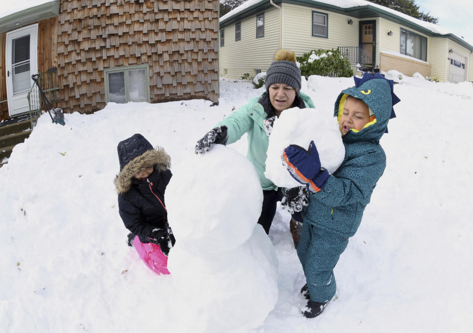 Arlene Wolf helps her children, Verona, 7, left, and Portor, 3, build a snowman in front of their home Friday, Oct. 11, 2019 in Bismarck, N.D. North Dakota Gov. Doug Burgum on Friday activated the state's emergency plan due to what he called a crippling snowstorm that closed major highways and had farmers and ranchers bracing for the potential of huge crop and livestock losses. (Mike McCleary/The Bismarck Tribune via AP)