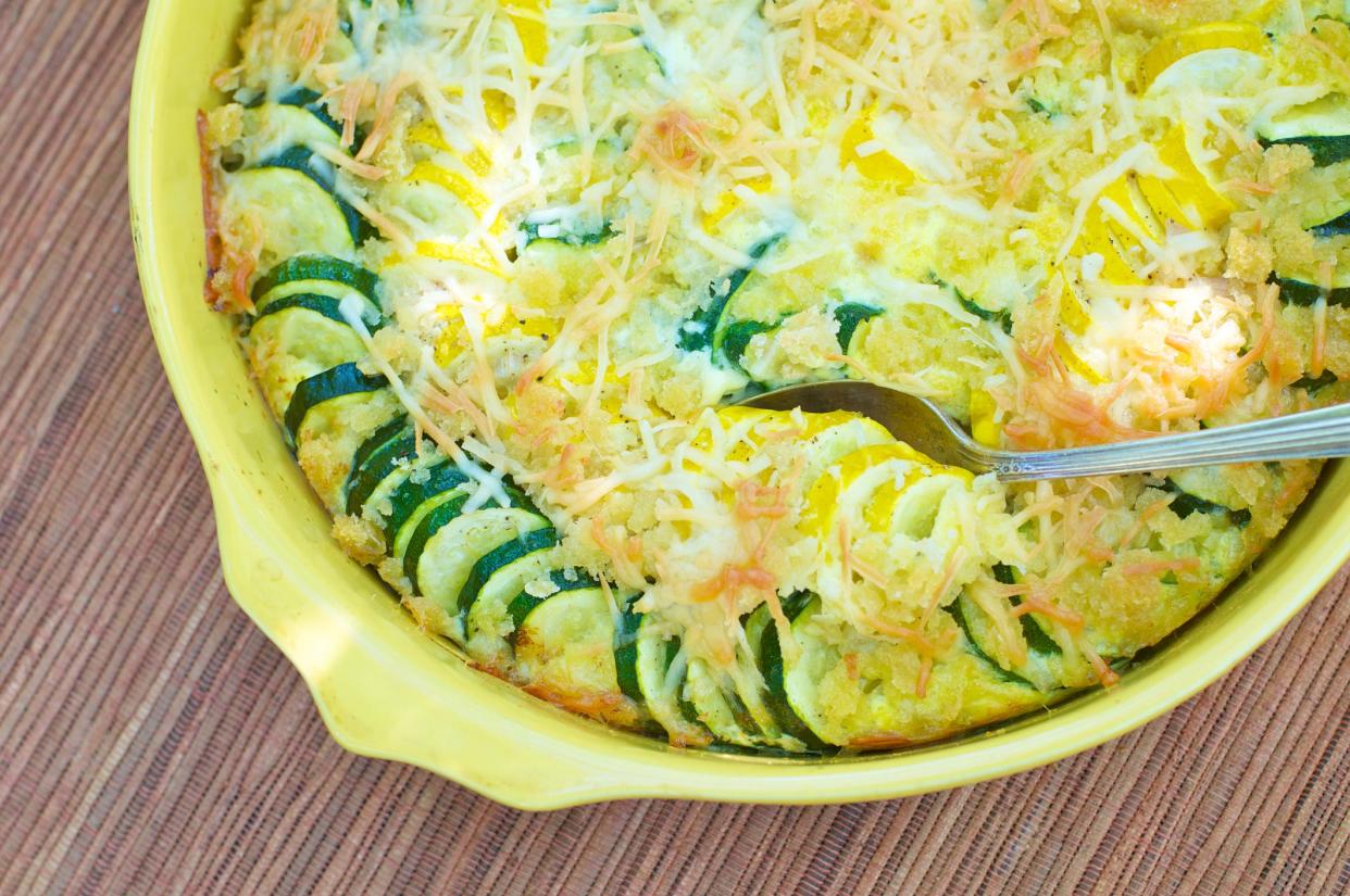 Yellow baking dish of summer squash casserole with spoon from above.