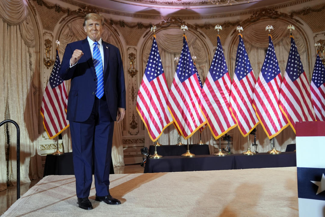 Former President Donald Trump, with a slew of U.S. flags behind him, pumps his fist at a Super Tuesday party at Mar-a-Lago.