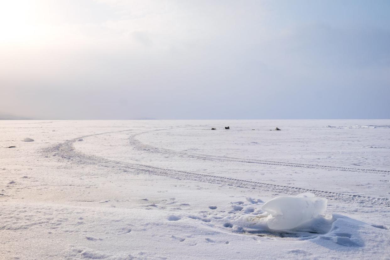 An ice cube on frozen lake covering with snow and tire marks during the sunset