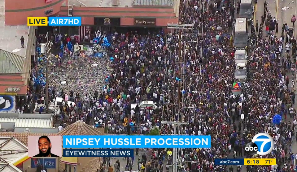 This photo taken from video provided by ABC7 shows thousands of people around the memorial and shrine where rapper Nipsey Hussle was shot and killed in front of his clothing store The Marathon, left, and the hearse, right, carrying his body in a casket draped in the flag of his father’s native country, Eritrea in East Africa, Thursday, April 11, 2019, in South Los Angeles. Hussle was remembered at a packed memorial service earlier Thursday held in Los Angeles’ Staples Center. (ABC7 via AP)