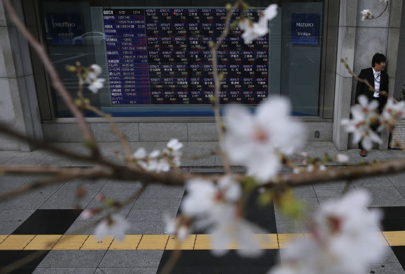 FILE PHOTO - A man stands next to an electronic stock quotation board as cherry blossoms are in full bloom outside a brokerage in Tokyo March 25, 2013. REUTERS/Issei Kato