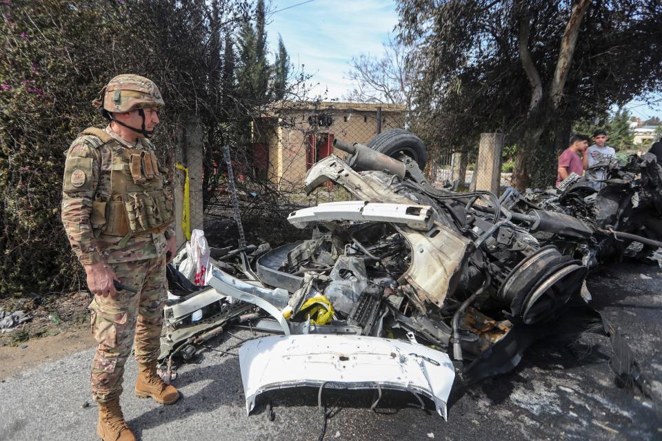 A Lebanese army officer stands next to a car destroyed in a drone strike that killed a Hamas leader in the southern outskirts of Tyre, Lebanon, on March 13, 2024.