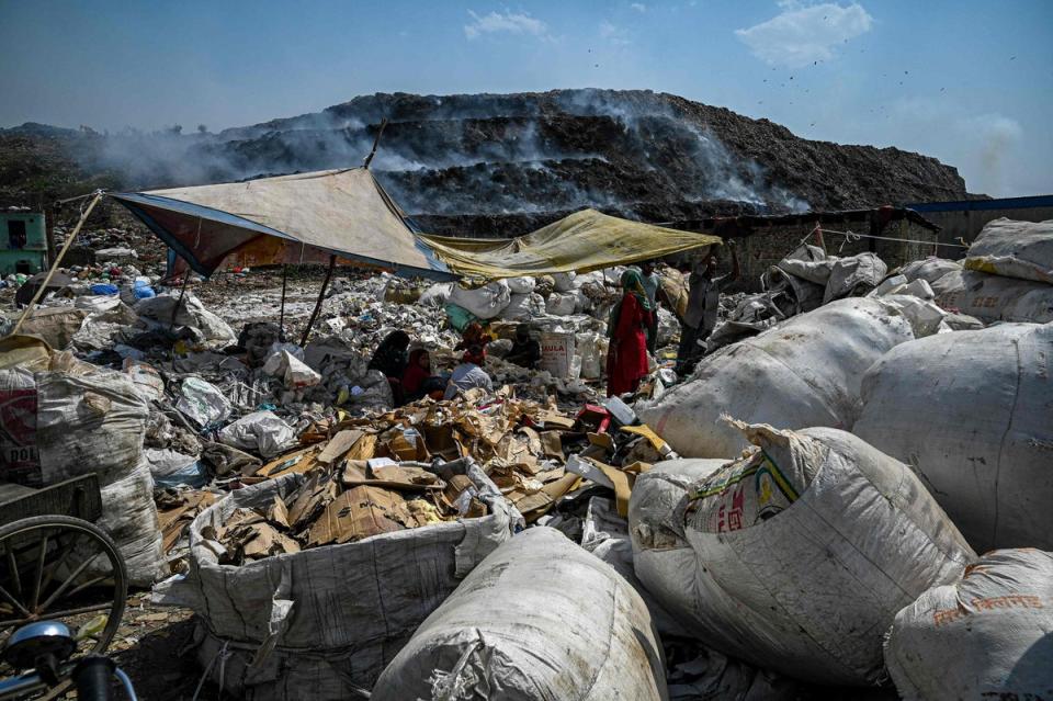 Workers segregate plastic, polythene and other reusable materials from waste collected by ragpickers as smoke billows during a fire at Bhlaswa landfill in New Delhi on 4 June 2022 (Getty)