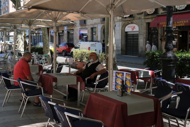 Un camarero se sienta en la terraza en la que trabaja a la espera de clientes, después de que el Gobierno de Cataluña anunciase restricciones para contener la propagación del virus