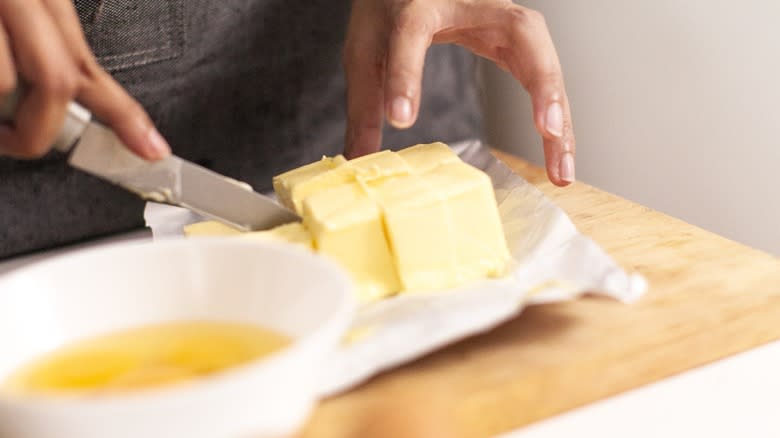 Hands cutting butter on a wooden board