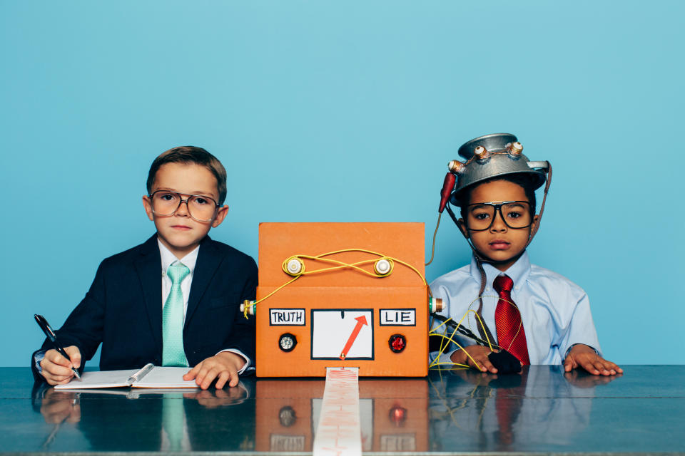 Two young boys and businessmen dressed in suits and glasses sit at a desk with a homemade lie detector machine. This serious interview is conducted in an office and the machine is predicting a lie from the job candidate. Dishonesty will eventually catch up to you.