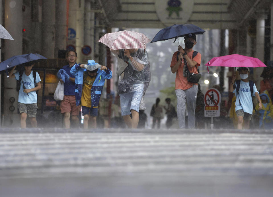 People walk across an intersection in a storm in Kagoshima, southern Japan, Tuesday, Aug. 8, 2023. Early Tuesday morning, the storm was centered 350 kilometers (217 miles) south of Kagoshima, a city on the southwestern tip of Japan’s main southern island of Kyushu. Khanun produced winds of 108 kph (67 mph) with gusts to 144 kph (89 mph) and was slowly moving north, the Japan Meteorological Agency reported. (Kyodo News via AP)