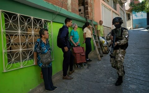 Residents stand near a wall as they watch a member of the FAES unit patrol the neighbouhood - Credit: Rodrigo Abd/AP